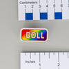 NerdyKeppie "DOLL" Mirrored Pride Pin. Mirrored pride pin with "DOLL" text in your choice of Progress, rainbow, or transgender pride colors. Say it with your whole chest.