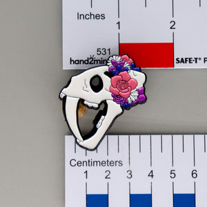NerdyKeppie Proud to the Bone Sabertooth Tiger Skull Pride Enamel Pins. A Sabertooth Tiger skull pride enamel pin for our Proud to the Bone project, a perfect prehistoric gift for your favorite nerd. This prehistoric pin wears an adorable flower crown!