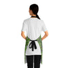 A person wearing a NerdyKeppie Lemurs Progress Pride Apron With Pocket. A sturdy poly twill apron with a pattern of lemurs and foliage on it. This pride pocket apron has an adjustable neck and two pockets.