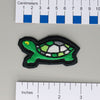 NerdyKeppie's Painted Turtle Embroidered Pride Patch are shaped like their namesake and stitched on black duck cloth!