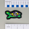 NerdyKeppie's Painted Turtle Embroidered Pride Patch are shaped like their namesake and stitched on black duck cloth!