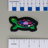 NerdyKeppie's Painted Turtle Embroidered Pride Patch are shaped like their namesake and stitched on black duck cloth!