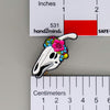 NerdyKeppie Proud to the Bone Parasauralophus Skull Pride Enamel Pins. A Parasauralophus skull pride enamel pin for our Proud to the Bone project. This prehistoric pin is wearing an adorable crown of flowers!