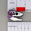 NerdyKeppie Proud to the Bone Tyrannosaurus Rex Skull Pride Enamel Pins. A Tyrannosaurus Rex skull pride enamel pin for our Proud to the Bone project. This prehistoric T-Rex pin is wearing an adorable crown of flowers!