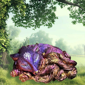 A purple, pink, orange, and gold kitsune figurine with a silver sigil on her forehead, asleep and photoshopped into a sunny meadow. The details on her face, the tips of her tails and her paws are all hand-painted. 