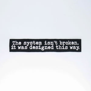 NerdyKeppie's "The System Isn't Broken It Was Designed This Way" Embroidered Patch are stitched on sturdy rectangular duck cloth and backed with vinyl fuse.
