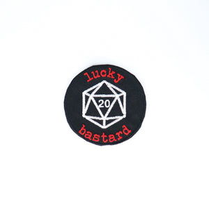 NerdyKeppie's White "Lucky Bastard" With D20 Embroidered Patch are stitched on black duck cloth and backed by sturdy vinyl fuse.